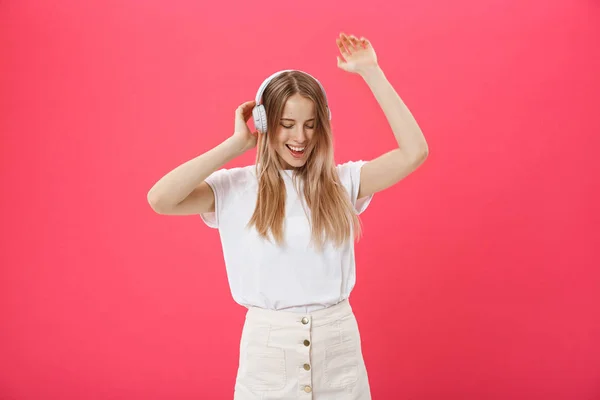 Komik kadın dans şarkı ve pembe bir arka plan üzerinde izole bir akıllı telefondan müzik dinlerken kulaklık ile. — Stok fotoğraf