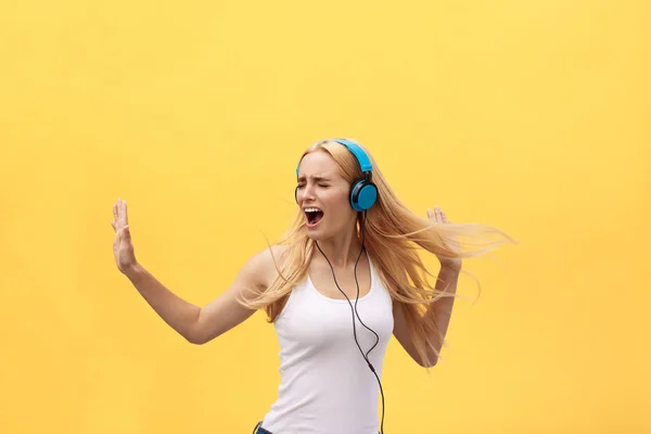 Lifestyle Concept: Retrato de una mujer alegre en camiseta blanca y escuchando música con auriculares mientras baila y canta aislada sobre fondo amarillo — Foto de Stock
