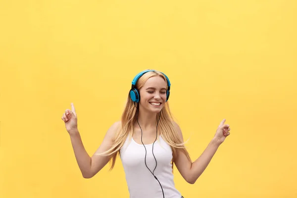 Lifestyle Concept: Retrato de una mujer alegre en camiseta blanca y escuchando música con auriculares mientras baila y canta aislada sobre fondo amarillo — Foto de Stock