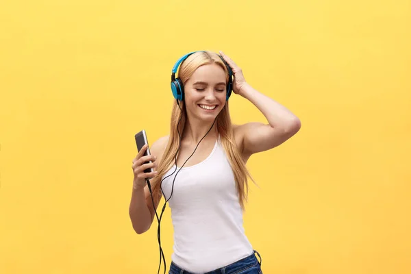 Lifestyle Concept : Portrait d'une femme joyeuse en t-shirt blanc et écouter de la musique avec des écouteurs tout en dansant et en chantant isolé sur fond jaune — Photo