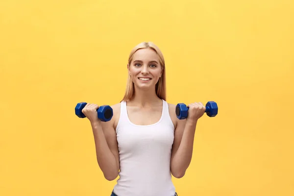 Portrait of pretty sporty girl holding weights and smiling. Isolated over yellow background. — Stock Photo, Image