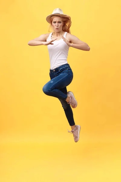 Young woman jump karate kicking in mid air isolated over yellow summer background
