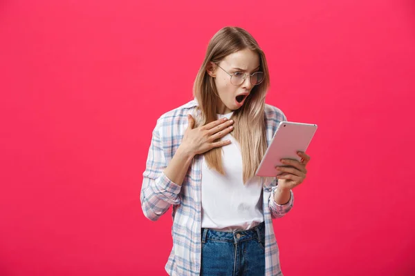 震惊的妇女看着数字平板电脑与惊喜和震惊的粉红色背景。在互联网上的惊讶或热门消息 — 图库照片