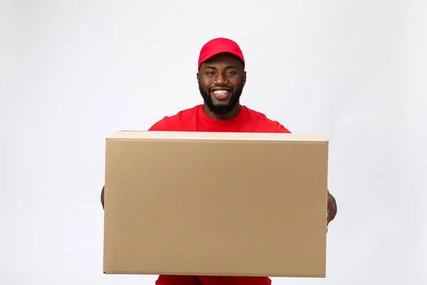 Conceito de entrega - Bonito homem de entrega afro-americano transportando caixa de pacote. Isolado no estúdio Grey Background. Espaço de cópia — Fotografia de Stock