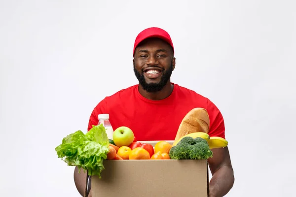 Delivery Concept - Fešák Afroameričan doručovatel nesoucí balíček potravin a nápojů ze skladu. Izolované na pozadí studia Grey. Kopírovat mezeru — Stock fotografie