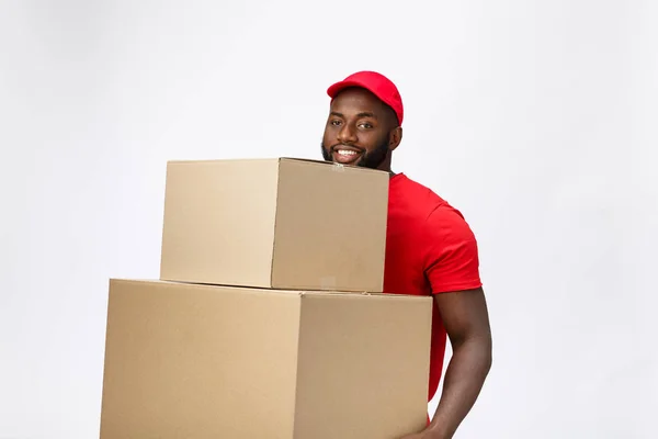 Koncepcja dostawy - Widok z boku Portret Happy African American dostawcą w czerwonej tkaninie trzymając paczkę pudełka. Odizolowany na szarym tle. Przestrzeń kopiowania — Zdjęcie stockowe