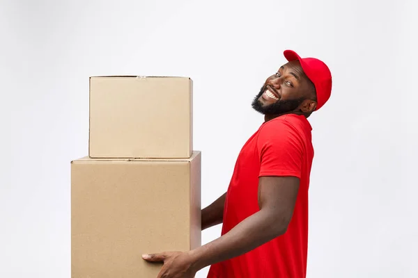 Retrato da entrega homem americano africano em camisa vermelha. ele levantando caixas de peso pesado contra ter um isolado no fundo branco . — Fotografia de Stock