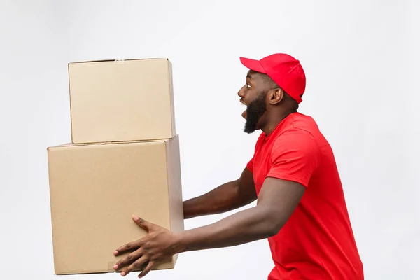 Retrato da entrega homem americano africano em camisa vermelha. ele levantando caixas de peso pesado contra ter um isolado no fundo branco . — Fotografia de Stock