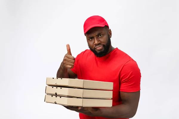 Concept de livraison - Portrait du livreur afro-américain heureux tenant un paquet de boîte à pizza et montrant pouces vers le haut. Isolé sur fond de studio Grey. Espace de copie — Photo