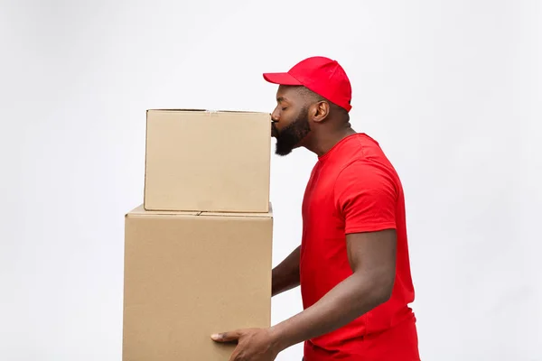 Delivery Concept - Side view Portrait of Happy African American delivery man in red cloth holding a box package. Isolated on Grey Background. Copy Space