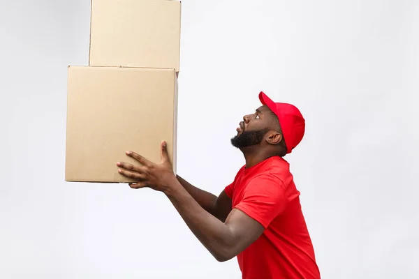 Lieferkonzept - Seitenansicht Porträt eines glücklichen afroamerikanischen Zustellers in rotem Tuch, der ein Karton-Paket hält. Isoliert auf grauem Hintergrund. Kopierraum — Stockfoto