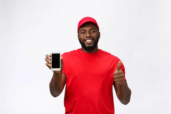 Delivery Concept - portré a boldog afro-amerikai kézbesítő férfi piros ruhával kezében egy doboz csomagot. Elszigetelve a szürke stúdió hátterében. Fénymásolási tér — Stock Fotó