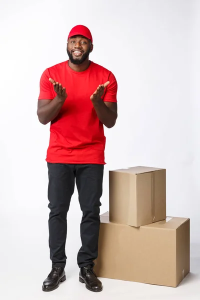 Концепція доставки - Портрет щасливого афроамериканця з доставки в червону тканину, що тримає коробковий пакет. Ізольовано на сірому фоні студії. Копіювати пробіл — стокове фото