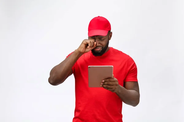 Delivery Concept - Portrait of Serious African American delivery man with tablet in silly aggressive expression and unhappy. Isolated on Grey studio Background. Copy Space