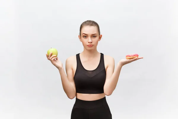 Mujer joven eligiendo entre donut y manzana sobre fondo blanco. Concepto de alimentación dietética —  Fotos de Stock