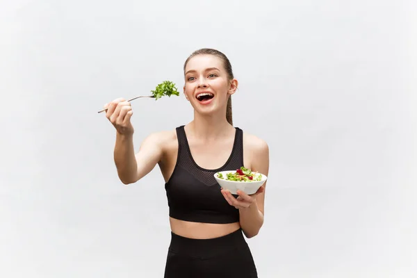 Young beautiful sport woman eating salad on white background.