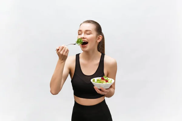 Young beautiful sport woman eating salad on white background.