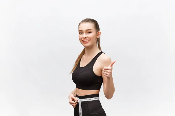 Retrato de mulher sorridente caucasiana atraente com fita métrica e mostrando o polegar isolado no fundo branco . — Fotografia de Stock