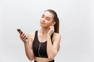 Genç sporcu kadının izole edilmiş görüntüsü sağlıklı atletik bir vücuda sahip, kulaklıkla müzik dinliyor, akıllı telefonu var. Gri arkaplan üzerinde izole.