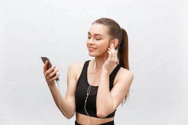 Genç sporcu kadının izole edilmiş görüntüsü sağlıklı atletik bir vücuda sahip, kulaklıkla müzik dinliyor, akıllı telefonu var. Gri arkaplan üzerinde izole.