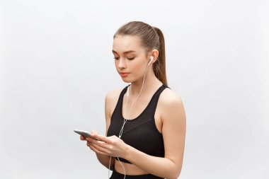 Genç sporcu kadının izole edilmiş görüntüsü sağlıklı atletik bir vücuda sahip, kulaklıkla müzik dinliyor, akıllı telefonu var. Gri arkaplan üzerinde izole.