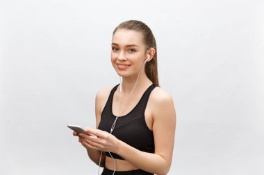 Genç sporcu kadının izole edilmiş görüntüsü sağlıklı atletik bir vücuda sahip, kulaklıkla müzik dinliyor, akıllı telefonu var. Gri arkaplan üzerinde izole.