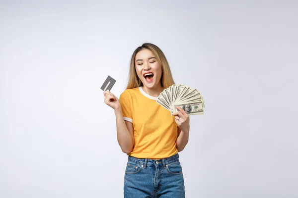 Азиатская контент-женщина держит фаната денег долларовые банкноты и кредитные карты и глядя на копирайт изолированы на сером фоне . — стоковое фото