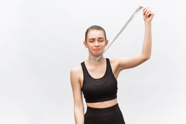 Üç mezurayla boyunu ölçen güzel, formda bir kız üzgün bir ifadeyle aşağıya bakıyor. Beyazda izole edilmiş