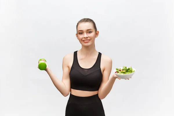 Sport, healthy lifestyle, people concept - young brunette woman with salad and a dumbbell. She is smiling and enjoying the healthy lifestyle.