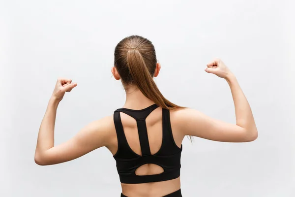 Waist up shot of sporty woman raises hand to show her muscles, feels confident in victory, looks stong and independent, smiles positively, stands against grey background. Sport concept — Stock Photo, Image