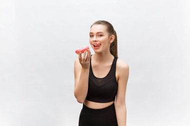 Güzel fitness modeli siyah bir fitness kıyafeti giyiyor ve elinde abur cubur var. Gri arkaplan üzerinde izole.