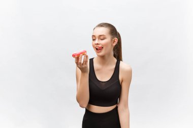 Güzel fitness modeli siyah bir fitness kıyafeti giyiyor ve elinde abur cubur var. Gri arkaplan üzerinde izole.