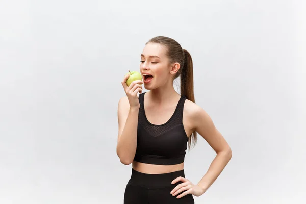 Portrait of a happy young caucasian woman holding and eating green apple over white background — Stock Photo, Image