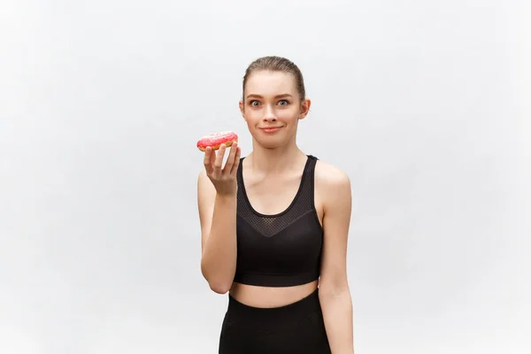 Modelo Fitness bonita vestindo uma roupa de fitness preto segurando um donut junk food. Isolado sobre fundo cinza . — Fotografia de Stock