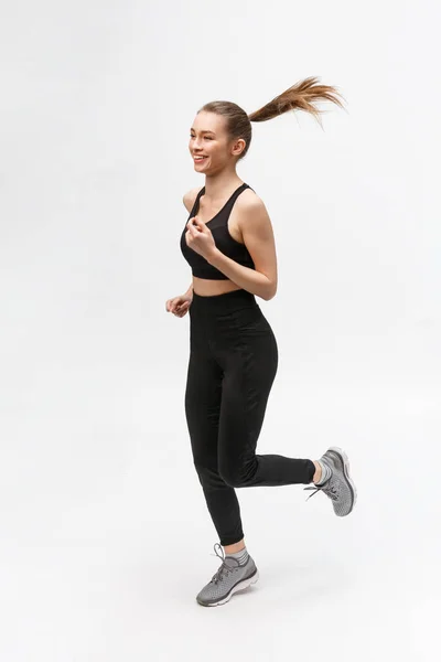 회색 배경을 배경으로 스튜디오에서 뛰고 있는 한 스포츠 여성의 전체 사진. — 스톡 사진