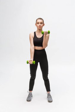 Beyaz arka planda beyaz kadın portresi siyah fitness giyiyor ve dambıllarla egzersiz yapıyor..