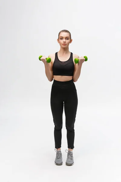 Retrato de mujer caucásica sobre fondo blanco usando fitness negro separado y haciendo ejercicio con pesas . — Foto de Stock