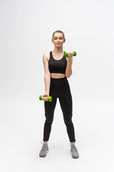 Retrato de mujer caucásica sobre fondo blanco usando fitness negro separado y haciendo ejercicio con pesas . — Foto de Stock