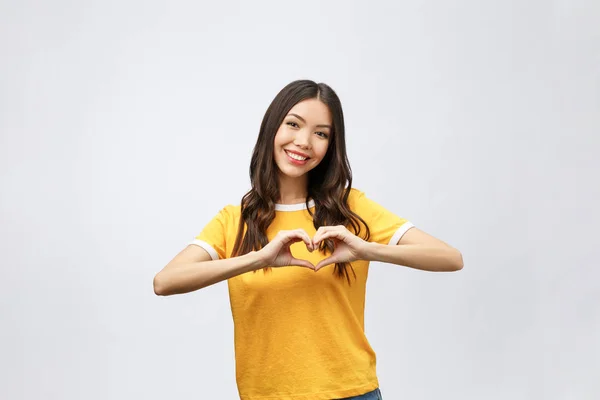 Porträt einer lächelnden jungen asiatischen Frau, die mit zwei Händen eine Herzgeste zeigt und isoliert vor weißem Hintergrund in die Kamera blickt. — Stockfoto