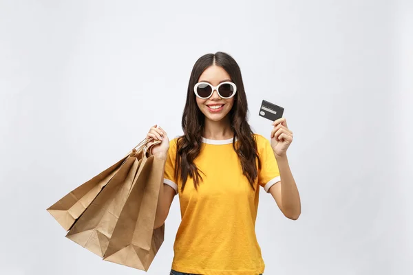 Close-up retrato de feliz jovem morena em óculos de sol segurando cartão de crédito e sacos de compras coloridos, olhando para a câmera, isolado no fundo branco — Fotografia de Stock