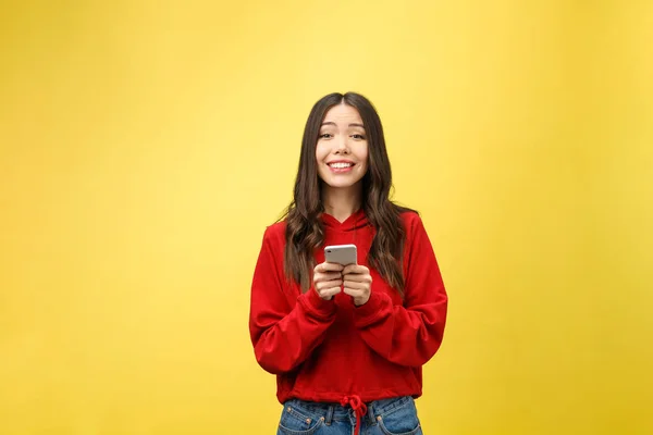 Joven hermosa mujer feliz usando el teléfono inteligente. Aislado sobre fondo amarillo — Foto de Stock