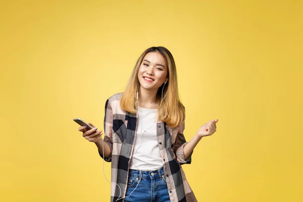 Fashion smiling asian woman listening to music in earphones over yellow background. — Stock Photo, Image