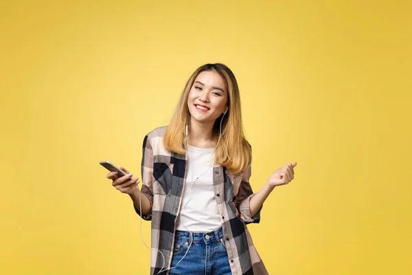 Moda sonriente mujer asiática escuchando música en auriculares sobre fondo amarillo . — Foto de Stock