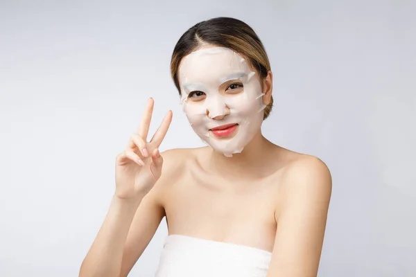 Beautiful asian woman applying paper sheet mask on her face white background. — Stock Photo, Image