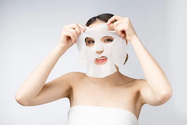 Beautiful asian woman applying paper sheet mask on her face white background — Stock Photo, Image