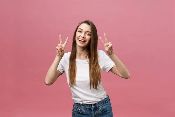 Retrato de una mujer alegre de moda mostrando dos dedos signo sobre fondo rosa —  Fotos de Stock