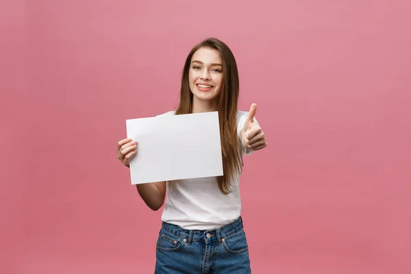Νεαρή γυναίκα ομορφιά κατέχουν λευκή κάρτα και δείχνει τους αντίχειρες πάνω από ροζ φόντο — Φωτογραφία Αρχείου