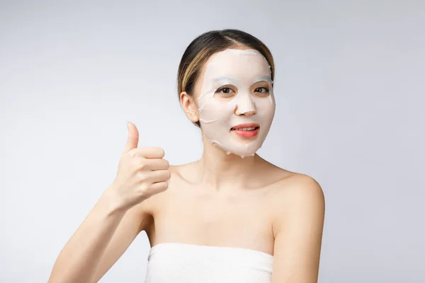 Спа, здравоохранение. Азиатка в косметической маске с большим пальцем вверх. — стоковое фото