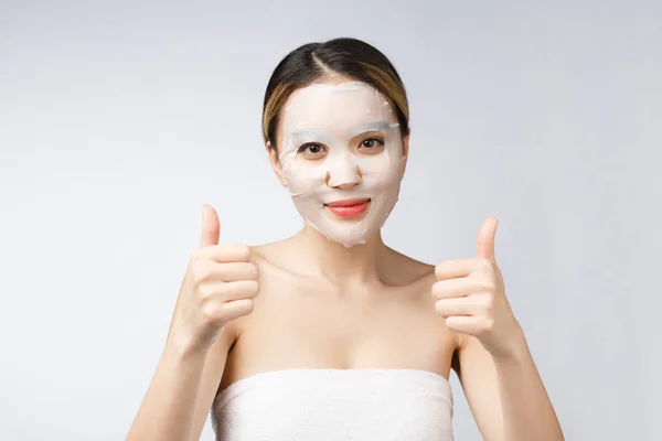 Lázně, zdravotní péče. Asijské dívka s kosmetickou maskou s ukazující palec nahoru. — Stock fotografie