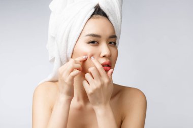 Yüzündeki sivilceye bakan Asyalı kadın. Genç kadın sivilcesini çıkarmaya çalışıyor. Kadın cilt bakım konsepti. Beyaz arkaplanda izole